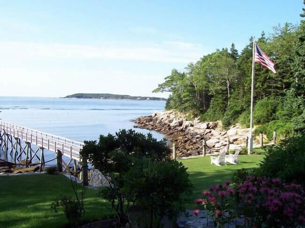 A coastal view with a wooden pier, a flag, and a grassy area with rocks.