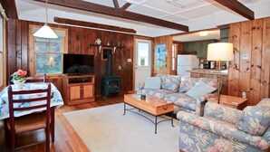 A cozy living room with wooden walls, a fireplace, a sofa, a television, and a dining area with a table and chairs. - Come and enjoy our Boothbay Cottage (Boothbay Harbor)