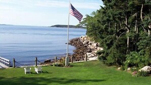 A grassy area with a flagpole, a chair, and a view of the water. - Come and enjoy our Boothbay Cottage (Boothbay Harbor)