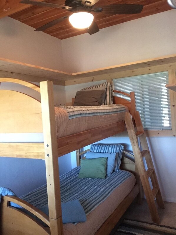 A bunk bed room with a wooden ladder, a ceiling fan, and a window with blinds.
