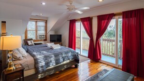 Ein Schlafzimmer mit einem Bett, einem Fernseher, einem Deckenventilator und einem Fenster mit roten Vorhängen.