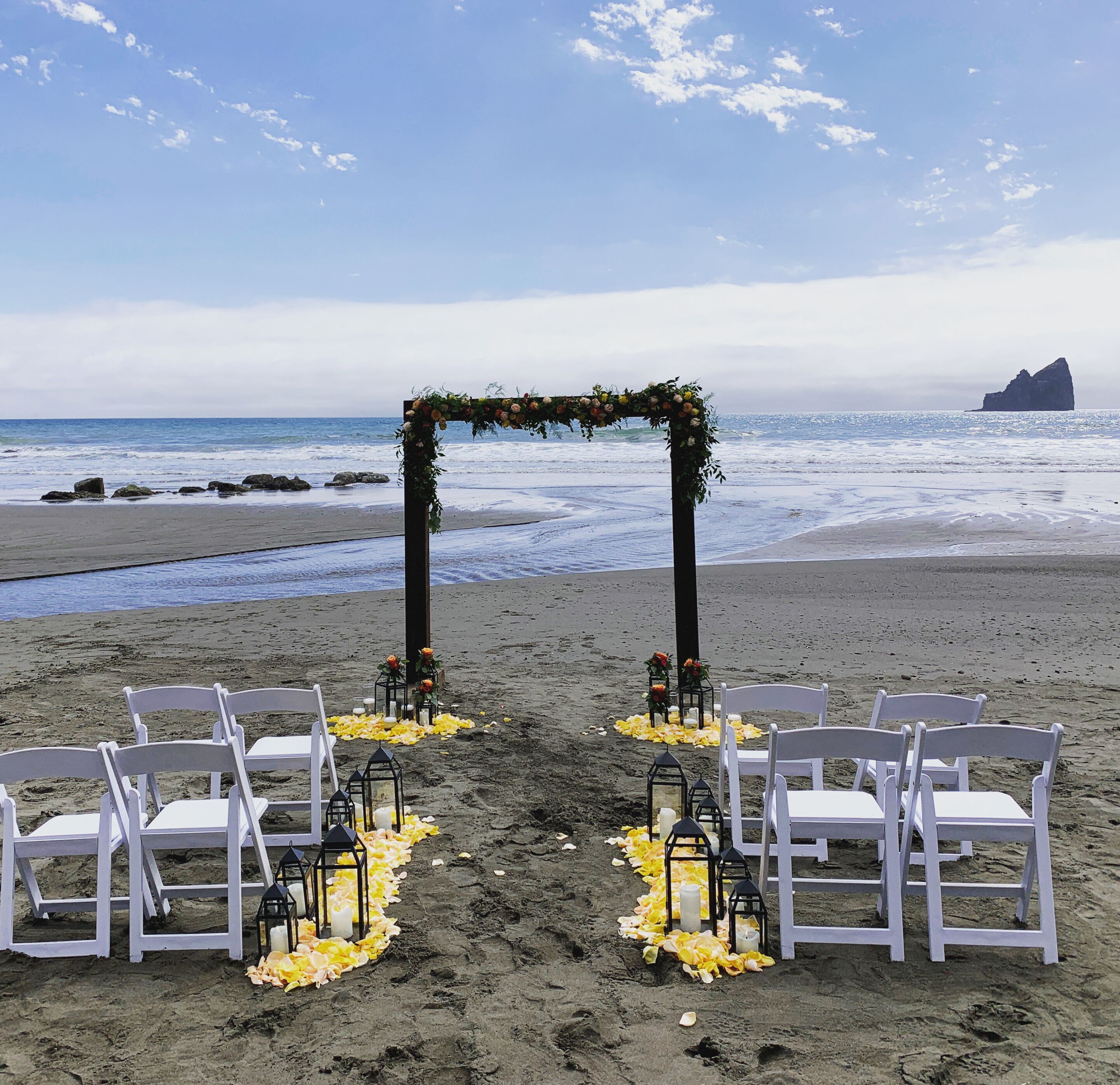 Une cérémonie de mariage organisée sur la plage, avec des chaises blanches et une arche décorée de fleurs.