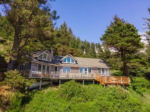 A wooden cabin with a deck, surrounded by dense forest. - Nautilus - Oceanfront Nantucket Style Home (Gold Beach)