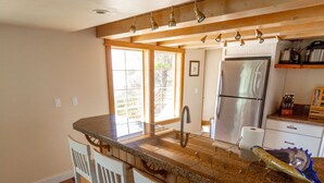 Cocina con encimera de granito, taburetes de bar blancos, refrigerador de acero inoxidable y ventana que proporciona luz natural.