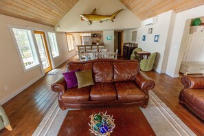 A spacious living room with a brown leather sofa, a coffee table with decorative glass balls, and a ceiling-mounted shark decoration. - Nautilus - Oceanfront Nantucket Style Home (Gold Beach)