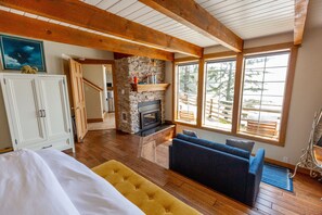 A cozy room with a stone fireplace, wooden beams, a sofa, and a bed. - Nautilus - Oceanfront Nantucket Style Home (Gold Beach)