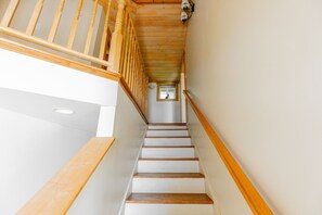 A wooden staircase with white steps and a wooden handrail, leading to a landing with a window. - Nautilus - Oceanfront Nantucket Style Home (Gold Beach)