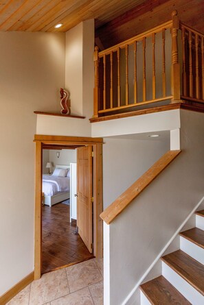 A wooden staircase with a white wall and a door leading to a bedroom with a bed and a nightstand. - Nautilus - Oceanfront Nantucket Style Home (Gold Beach)