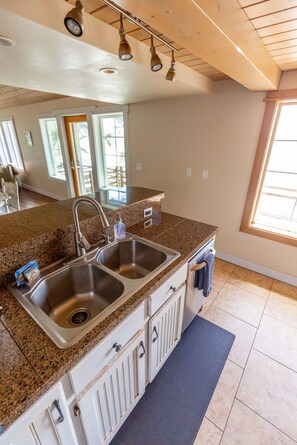 A kitchen with granite countertops, stainless steel sinks, and white cabinetry. - Nautilus - Oceanfront Nantucket Style Home (Gold Beach)