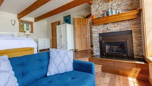 Un dormitorio con cama, un sofá azul, chimenea, vigas de madera y pared de piedra.