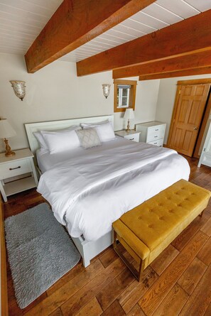 A bedroom with a large bed, bedside tables, a bench, and a wooden ceiling. - Nautilus - Oceanfront Nantucket Style Home (Gold Beach)