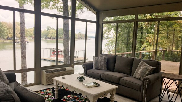 A living room with a large window overlooking a lake, a gray sofa, a white coffee table, and a colorful rug. - House on Lake Hamilton Sleeps 17 in beds (Hot Springs)