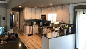 A spacious kitchen with white cabinets, a central island, stainless steel appliances, and a large window providing natural light. - House on Lake Hamilton Sleeps 17 in beds (Hot Springs)
