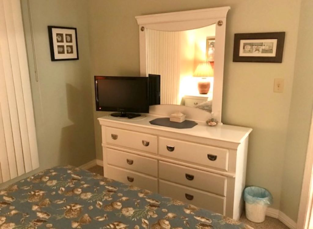 A bedroom with a bed, dresser, television, and framed pictures on the wall.