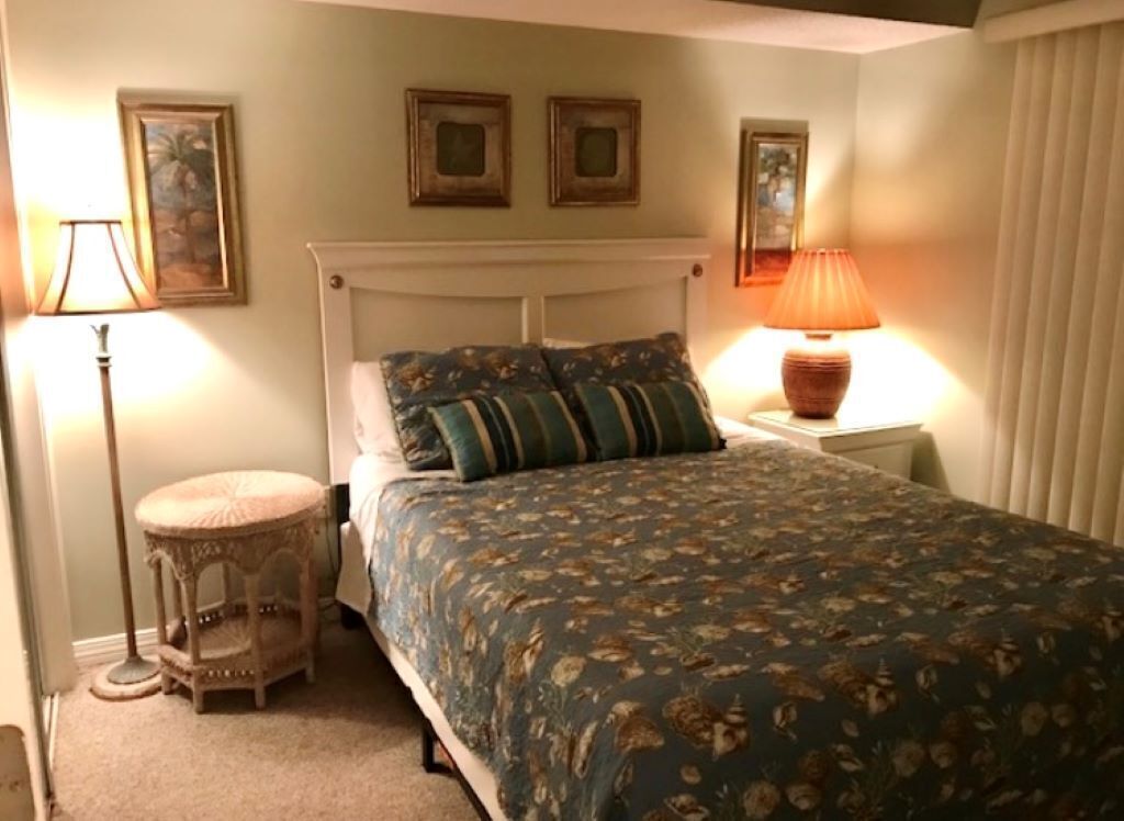 Ein Schlafzimmer mit einem Bett, zwei Nachttischlampen, einem kleinen runden Tisch und gerahmten Bildern an der Wand.