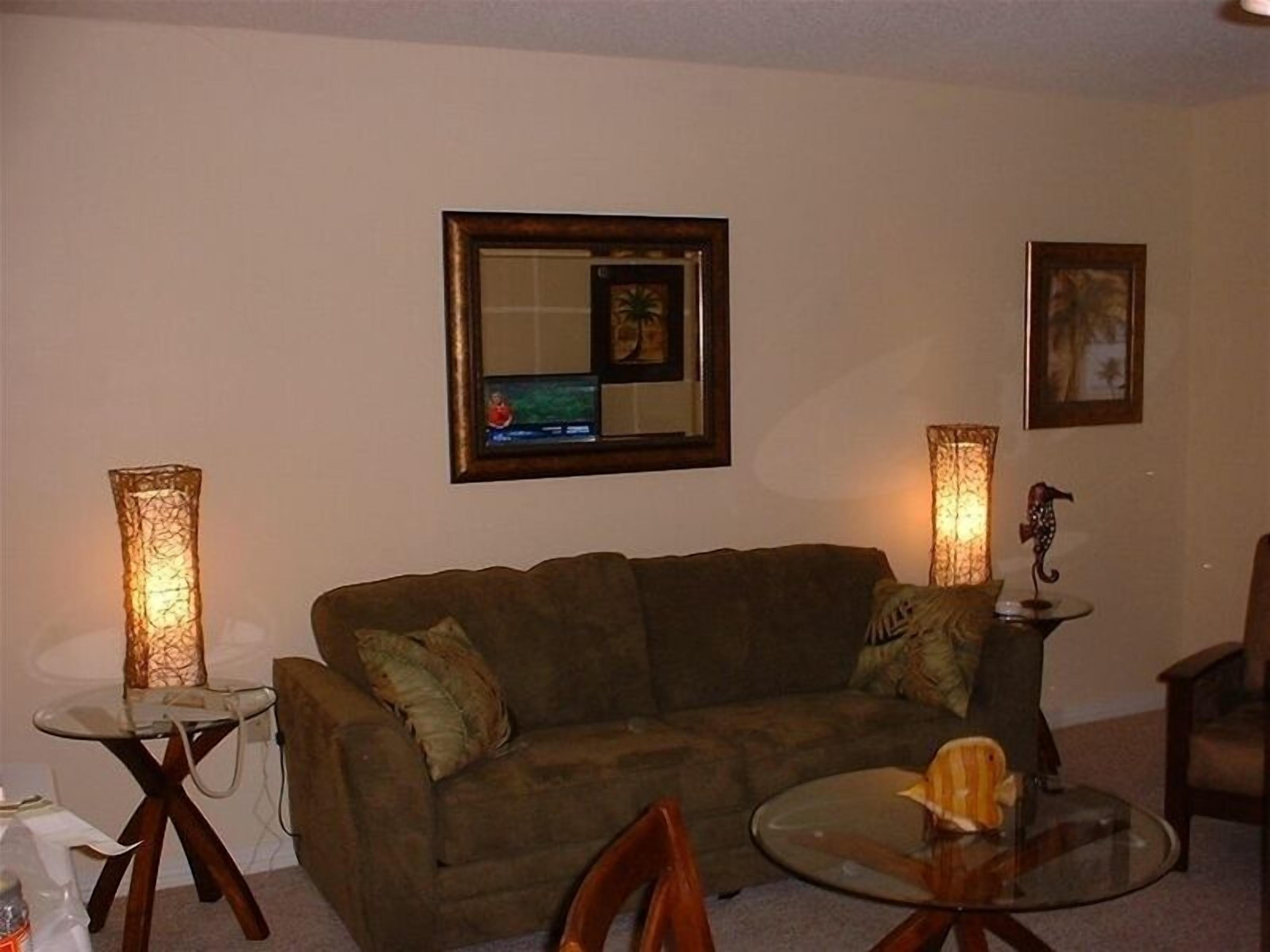 A living room with a brown sofa, a glass coffee table, and two tall lamps.