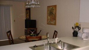 A kitchen with a double sink, a coffee maker, and a dining area with chairs and a table. - Low Rates ! Gulf View; Palms, Grnd Flr; Weekly discounts (Gulf Shores)