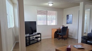 Amplia sala de estar con televisor de pantalla plana, una mesa de centro de madera, un sofá de cuero negro y un tapete estampado.