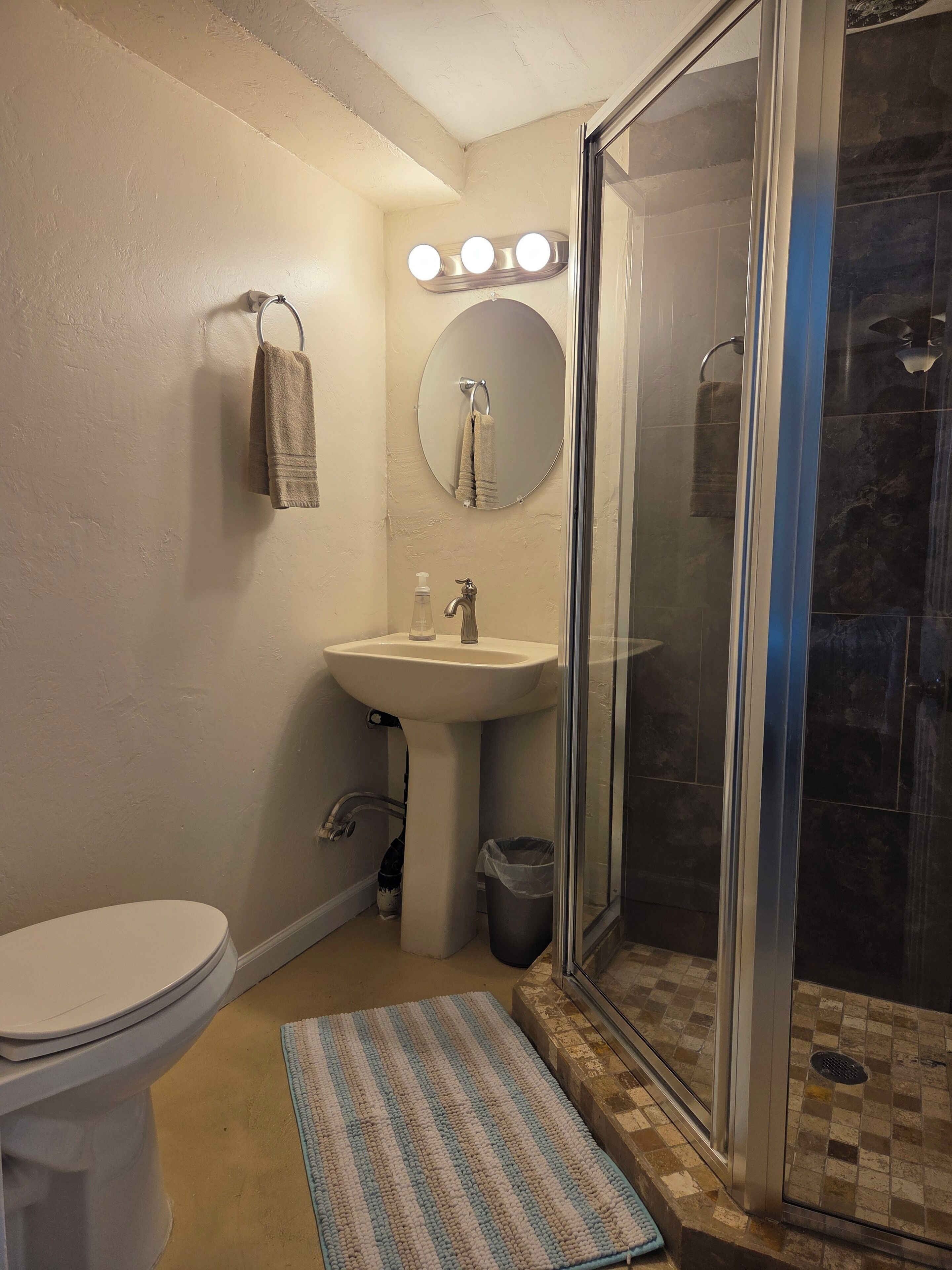 Un baño con inodoro, lavabo, espejo y cabina de ducha de vidrio.