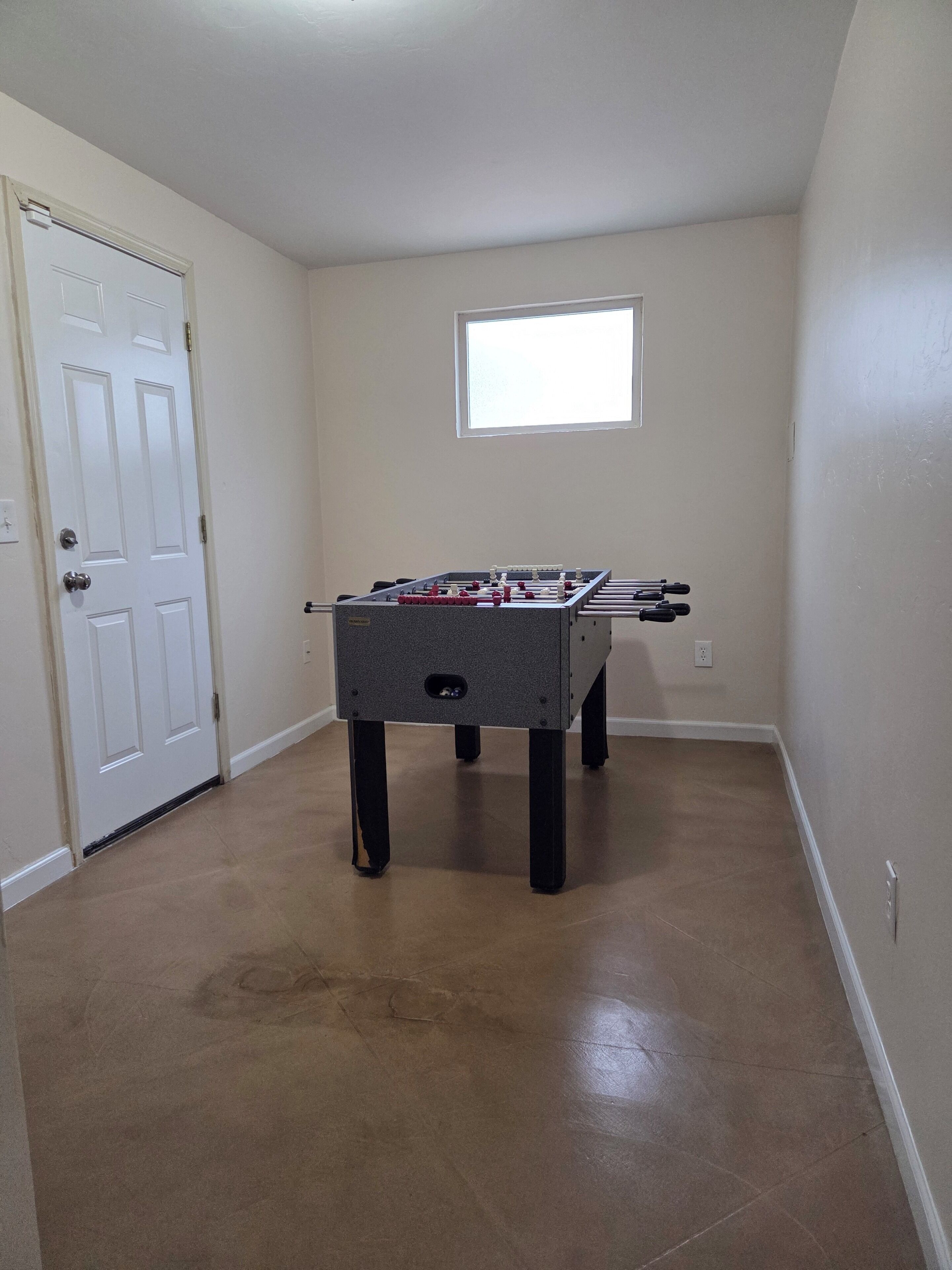 Una habitación con mesa de fútbol, una puerta y una ventana.