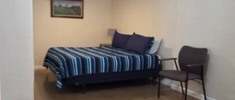 Un dormitorio con una cama, una silla, un ventilador de techo y un cuadro en la pared.