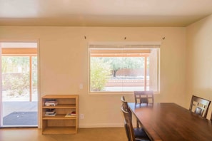 Enjoy meals at the large dining table with four chairs, surrounded by a bookshelf and two windows offering a view of the outdoors.