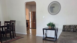 Una sala de estar con comedor, un sofá, una mesa de centro, un tapete, un espejo y una cocina al fondo.