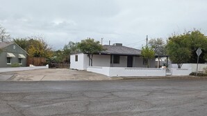 Una casa pequeña de un solo piso con fachada blanca y tejado gris.