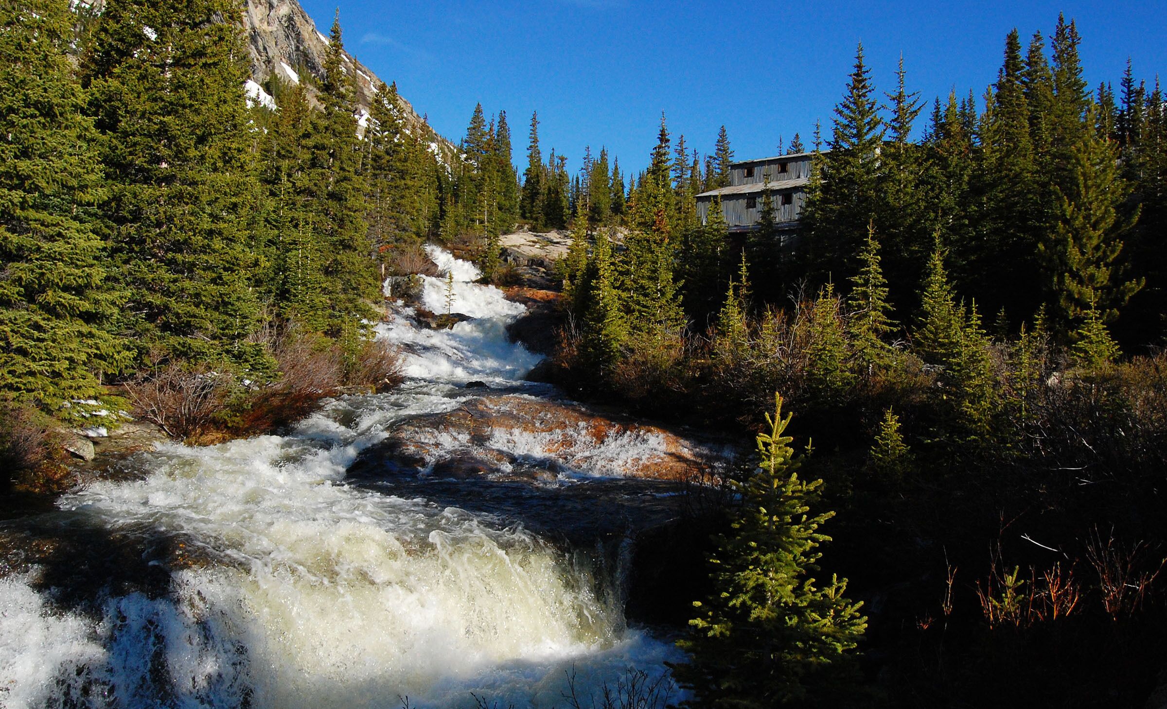 A waterfall in a forested area with a building in the background.