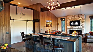 Une cuisine moderne dotée d’un îlot central, de tabourets de bar, d’une cheminée en pierre et d’un coin repas avec un canapé.