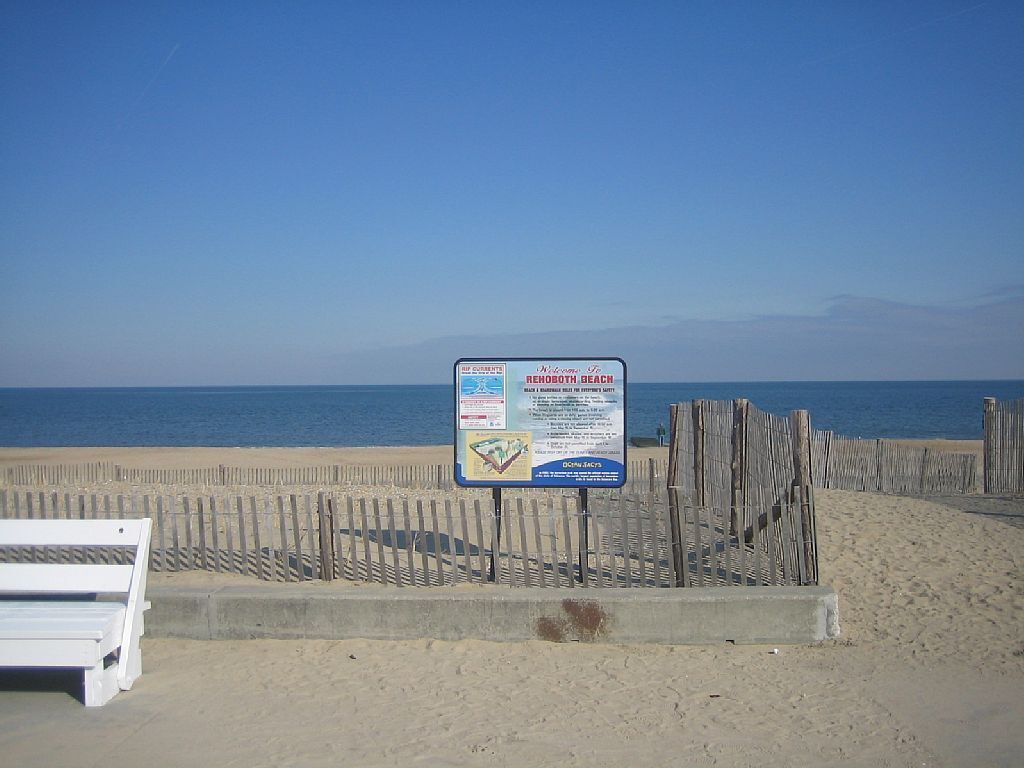 Un letrero de playa con información de seguridad y una valla de madera.
