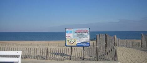 Un letrero de playa con información de seguridad y una valla de madera.