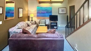 A cozy living room with a wooden ceiling, a ceiling fan, a sofa, a coffee table, and a TV. - River Vista Homes: Perfect for Fishing, Swimming, and Relaxing by the Water (Idleyld Park)
