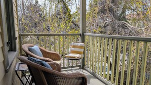 Un balcon abrité, doté de meubles en osier et offrant une vue sur les arbres et les arbustes.