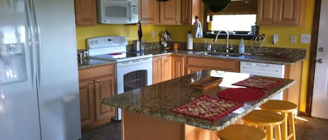 A kitchen with wooden cabinets, a white refrigerator, a stove, and a microwave. There are stools at the island and hanging pots above the stove.
