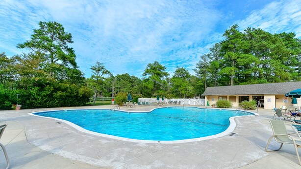 A swimming pool with a curved edge, surrounded by a paved deck and lounge chairs. - Bethany Beach 3-BR Townhouse With Pool and Tennis - Walking Distance to Beach! (Bethany Beach)