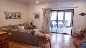 A living room with a sofa, chairs, a table, and a view through a glass door to an outdoor area. - Bethany Beach 3-BR Townhouse With Pool and Tennis - Walking Distance to Beach! (Bethany Beach)