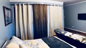 Une chambre à coucher avec un lit, des rideaux, un téléviseur et un tableau encadré au mur.