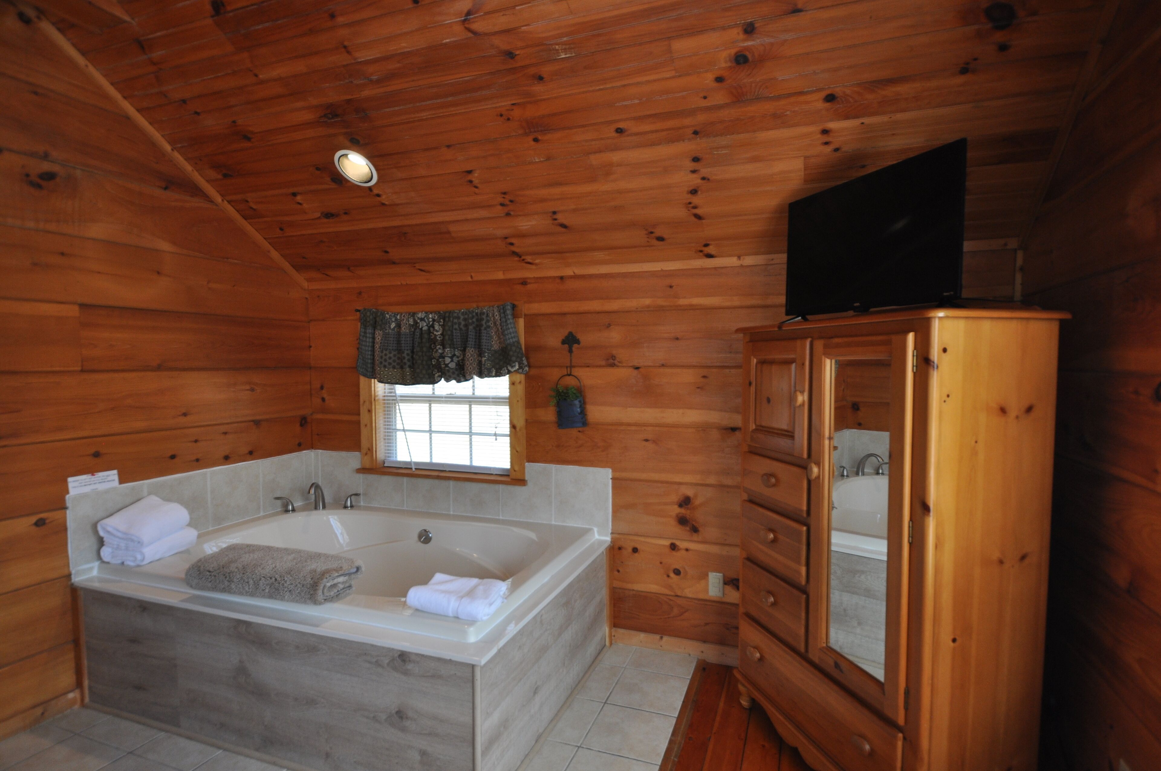 Bagno di una baita in legno con una vasca da bagno grande, mobili in legno e un televisore a parete.