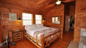 Un dormitorio de cabaña de madera con cama, mesita de noche, escritorio y ventilador de techo.