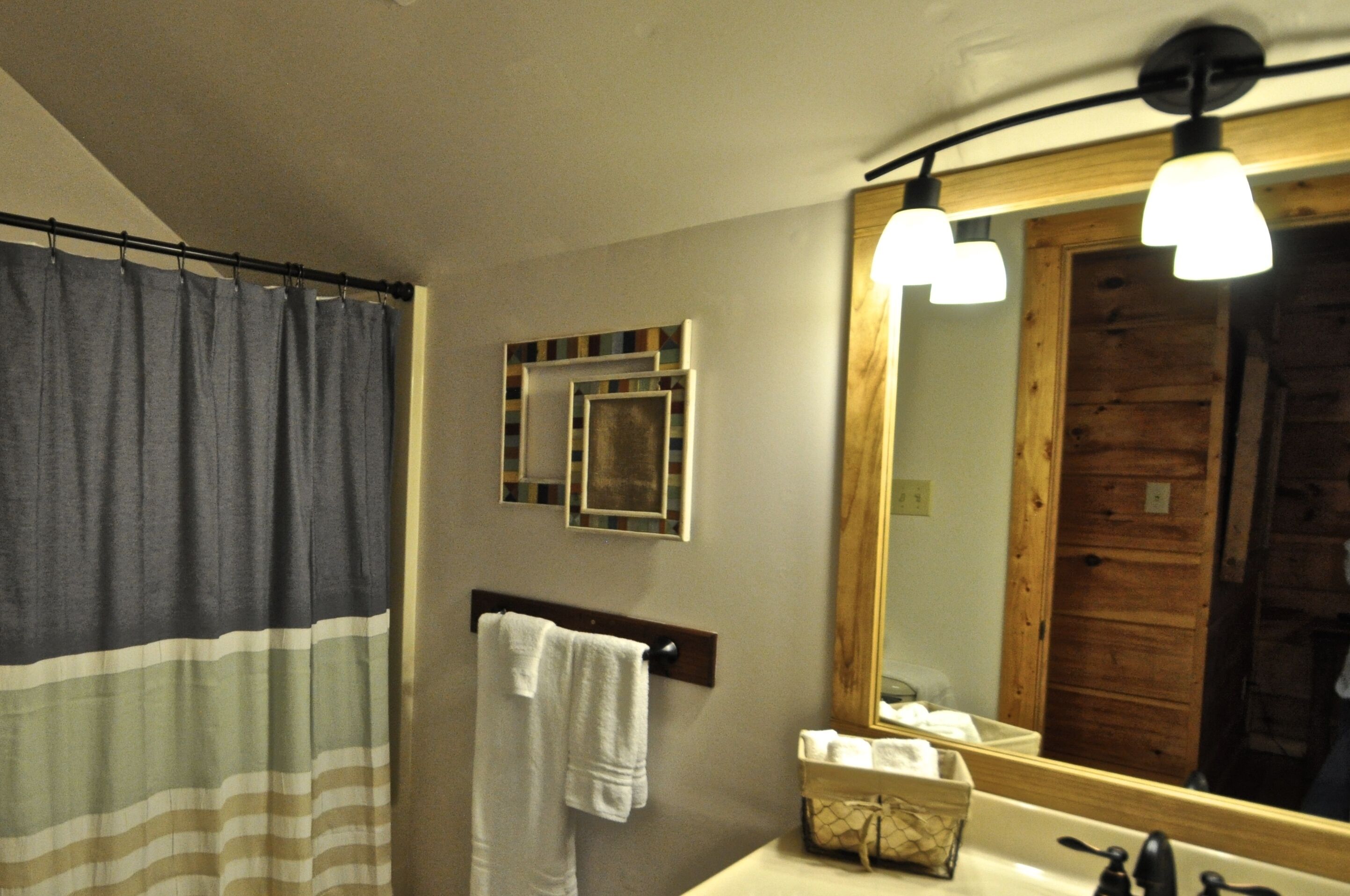 Un baño con cortina de ducha, un perchero con una toalla blanca, un espejo y un lavabo con dispensador de jabón.