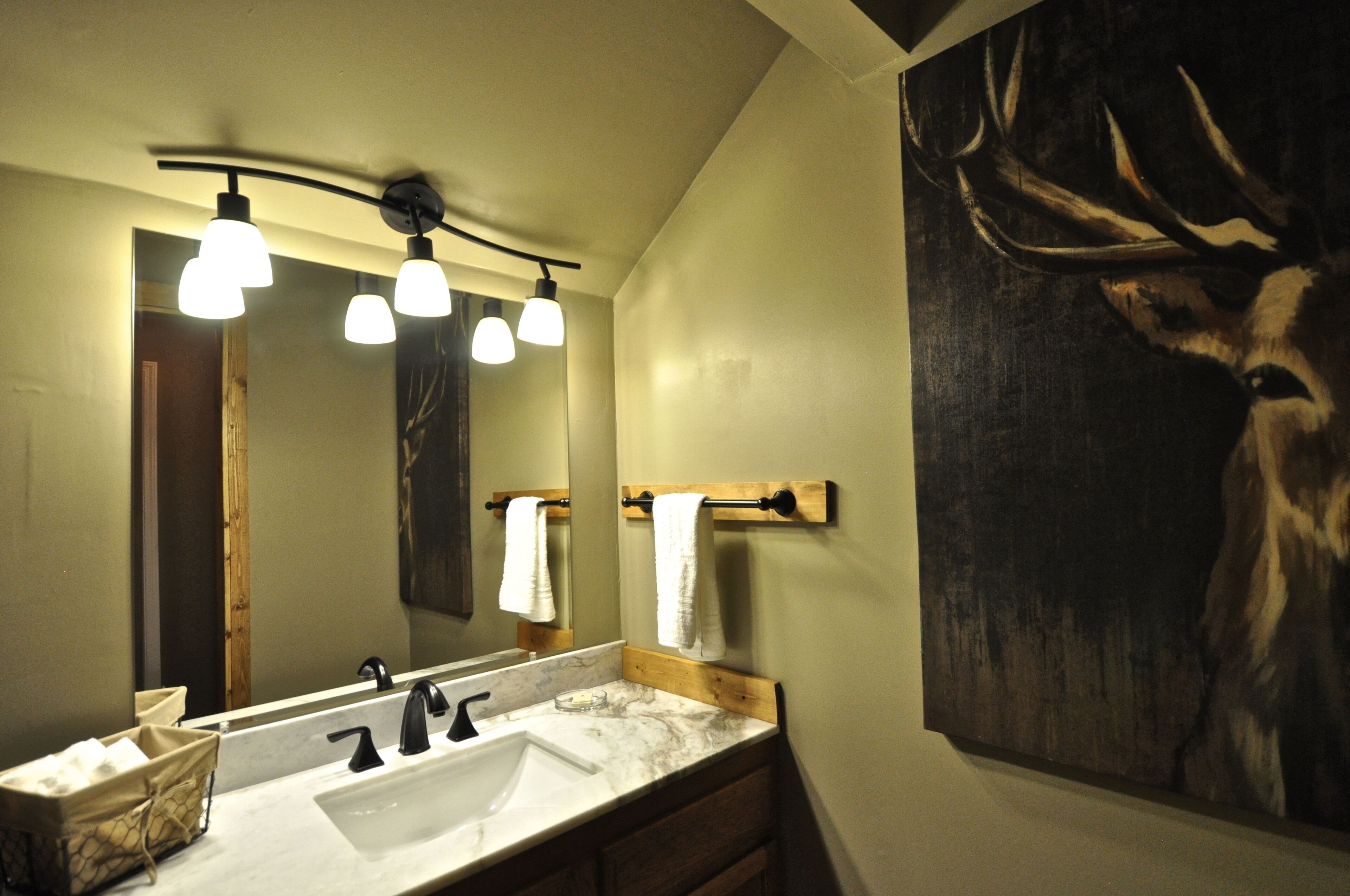 Une salle de bain avec un grand miroir, un lavabo et un tableau représentant un cerf accroché au mur.