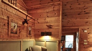 Interior acogedor de una cabaña con paredes de madera, un sillón cómodo, una mesita y una ventana que deja entrar luz natural.