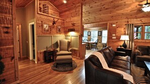Interior de una cabaña de madera con comedor, muebles de cuero y un ventilador de techo.