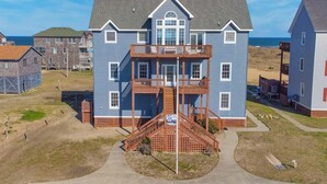 A two-story house with a balcony, a front porch, and a staircase leading to the second floor. - Oceanfront Dog Friendly Rodanthe Home w/ Pool, Hot Tub, Game Room, Home Theater (Rodanthe)