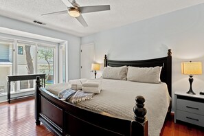 A bedroom with a bed, bedside lamps, a ceiling fan, and a view through a window. - Beachwalk Cottage – Steps to Beach, Free Seasonal Pool Heat, Sleeps 10, 4 King Suites (Hilton Head Island)