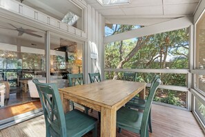 A dining area with a wooden table and chairs, large windows, and a view of trees. - Beachwalk Cottage – Steps to Beach, Free Seasonal Pool Heat, Sleeps 10, 4 King Suites (Hilton Head Island)