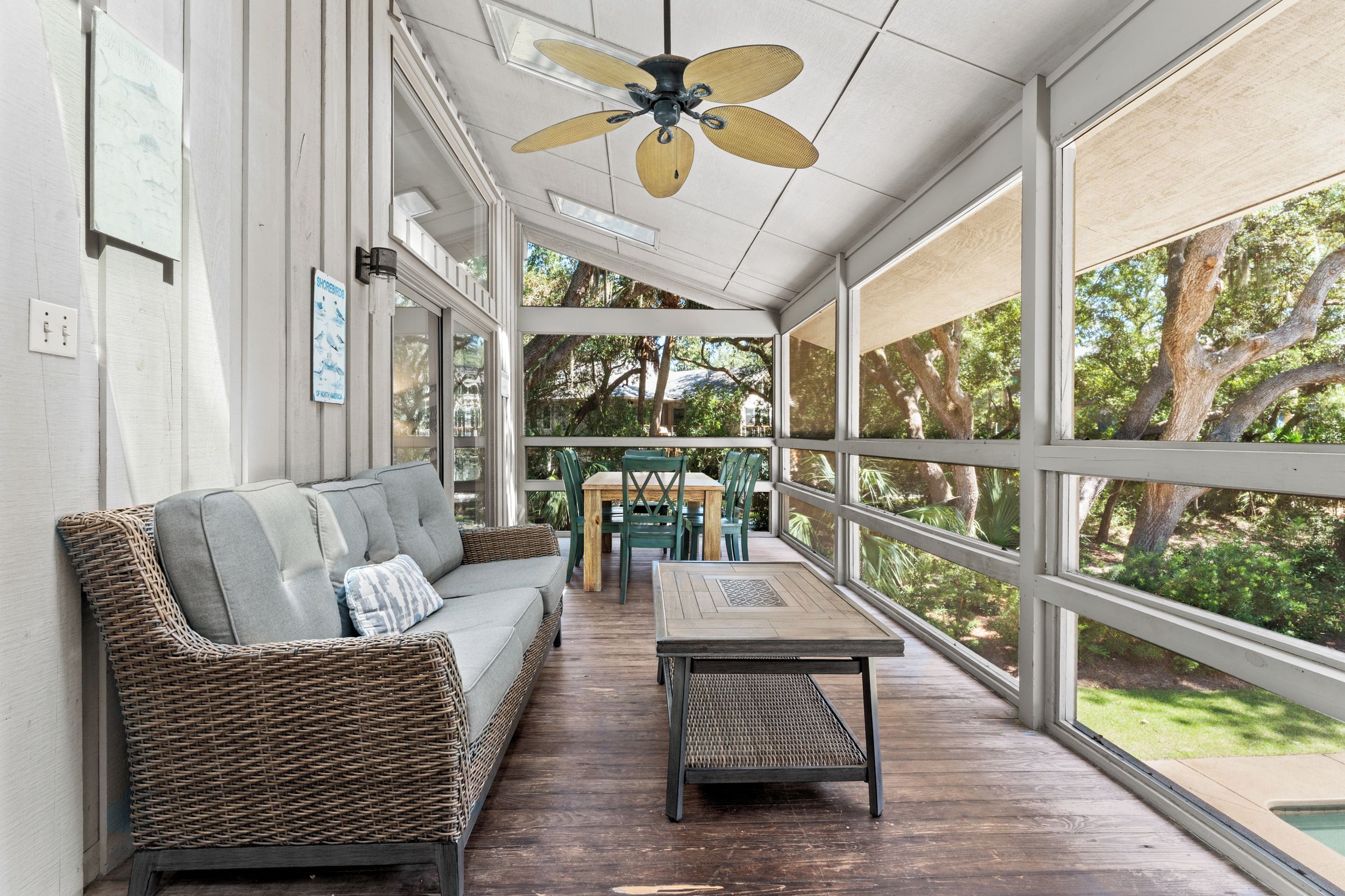 A covered outdoor area with a wicker sofa, a wooden table, and a ceiling fan.