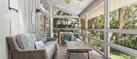 A covered outdoor area with a wicker sofa, a wooden table, and a ceiling fan.