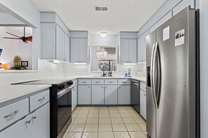 A modern kitchen with grey cabinets, a stainless steel refrigerator, and a dishwasher. - Beachwalk Cottage – Steps to Beach, Free Seasonal Pool Heat, Sleeps 10, 4 King Suites (Hilton Head Island)